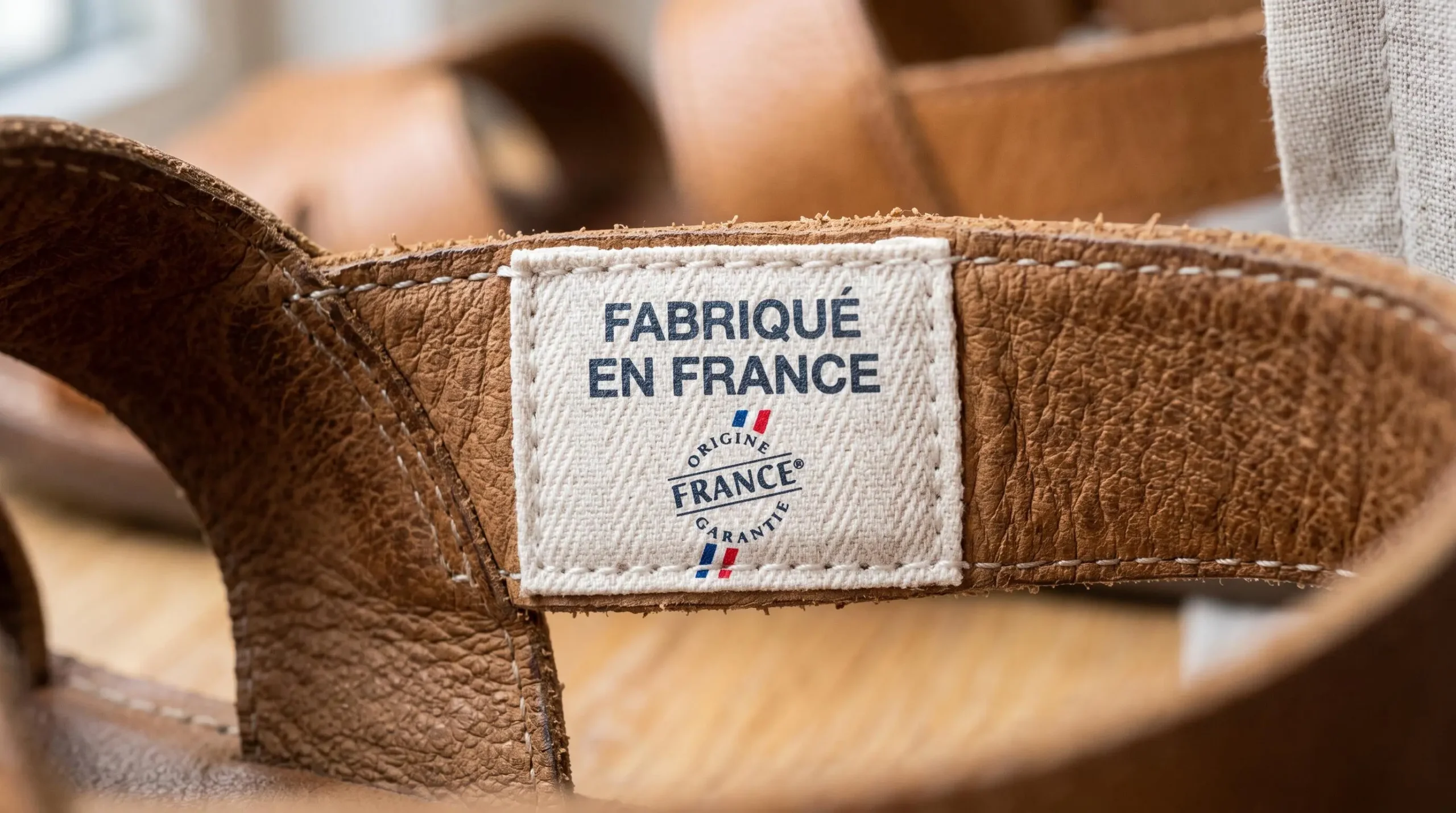 Gros plan sur étiquette textile 'Fabriqué en France' avec logo Origine France Garantie cousue sur bride intérieure d'une sandale en cuir camel